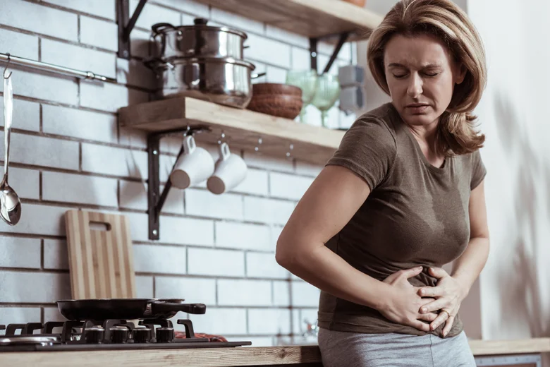 Žena v kuchyni s bolestí břicha po jídle