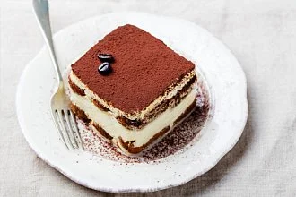 Kousek tiramisu posypaný kakaem na bílém talíři.