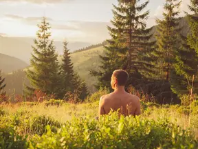 Muž sedí v přírodě mezi trávou a užíva si klidu.