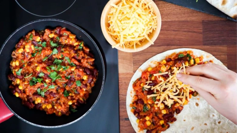 Příprava tacos s fazolemi a sýrem na dřevěném prknu.