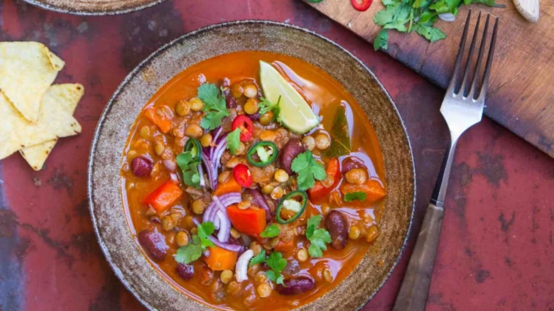Barevná veganská polévka z čočky s zeleninou v hrnci.