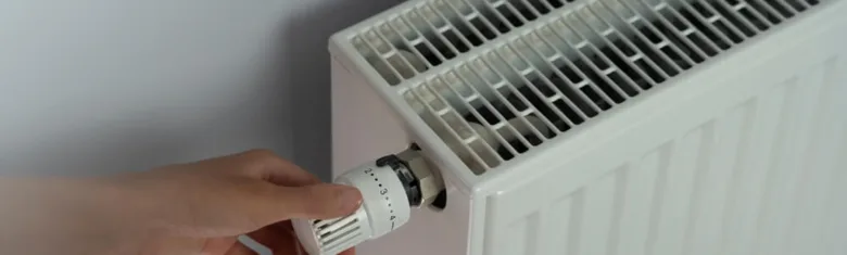 Ruka nastavuje termostat na radiátoru pro topení plynem.