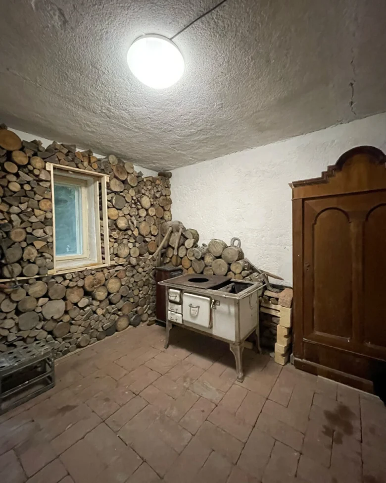 Interiér roubené chalupy s kamny a zásobou dřeva.