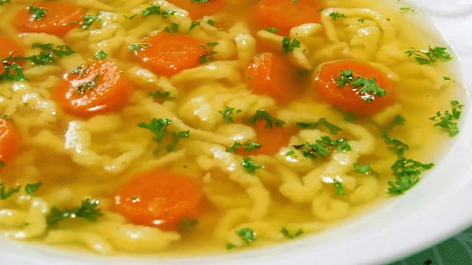 Hot carrot noodle soup garnished with fresh parsley.