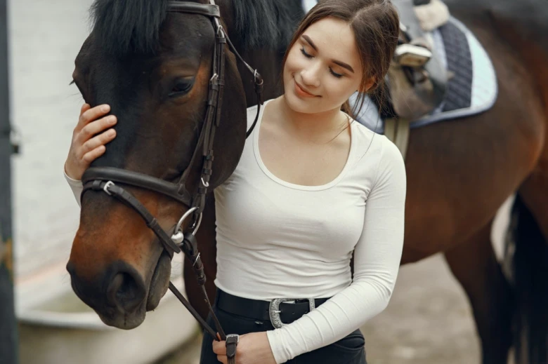 Mladá žena hladí hřebce v blízkém záběru.