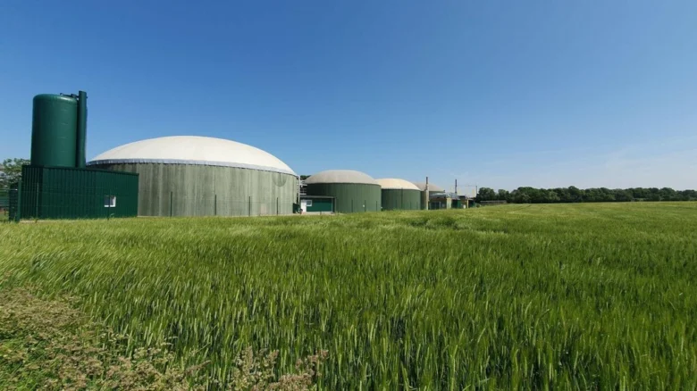 Domácí bioplynová stanice na pozadí zelené polní plochy.
