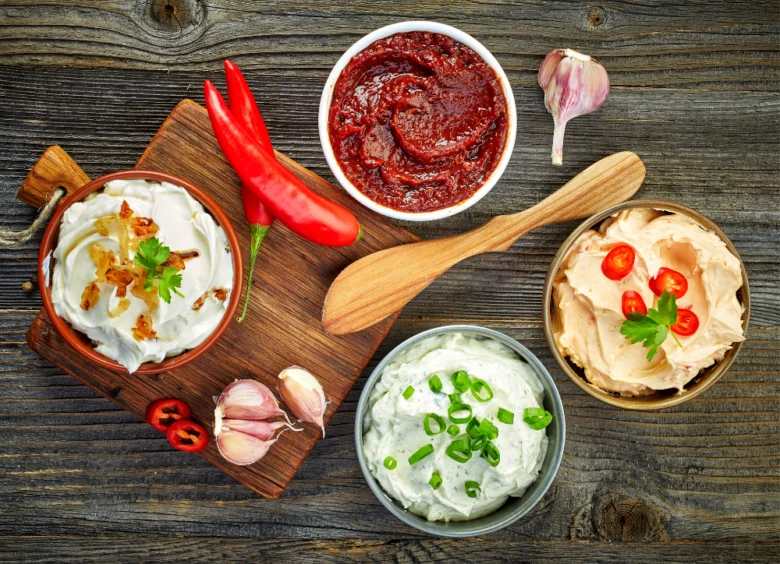Čtyři domácí dipy s čerstvými ingrediencemi na dřevěném povrchu.
