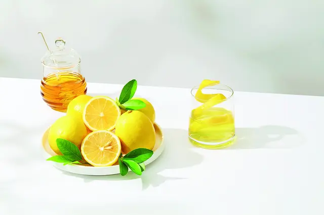Čerstvé citrony, med a sklenička s limonádou na bílém povrchu.