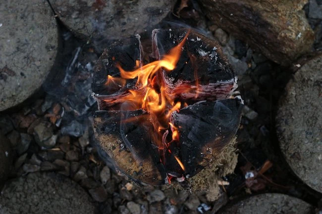 Zapálená švédská svíce z dřevěných kmenů na kamení.