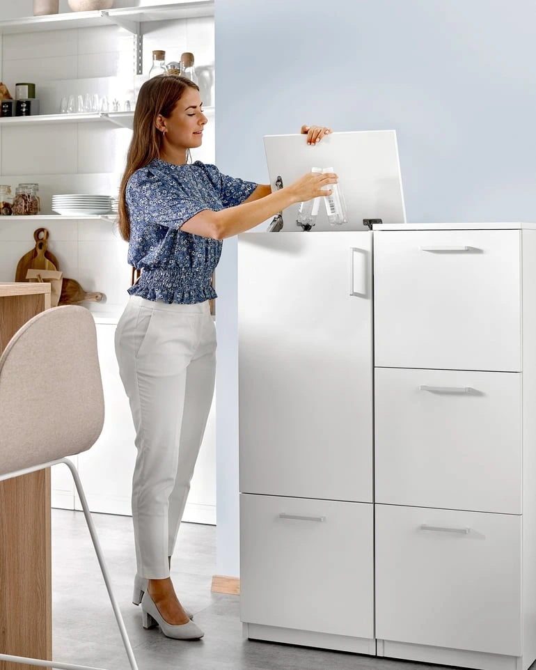 Žena ukládá plastové lahve do kuchyňského skříně na recyklaci.