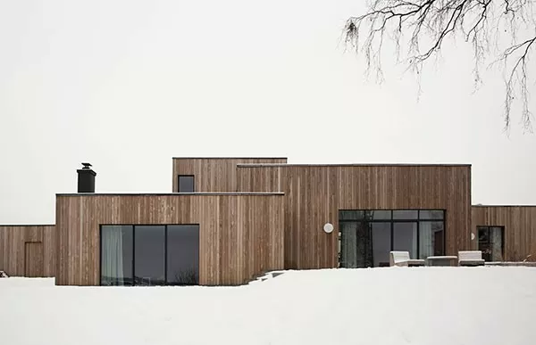 Moderní dům ve svahu s dřevěnou fasádou v zimním prostředí.