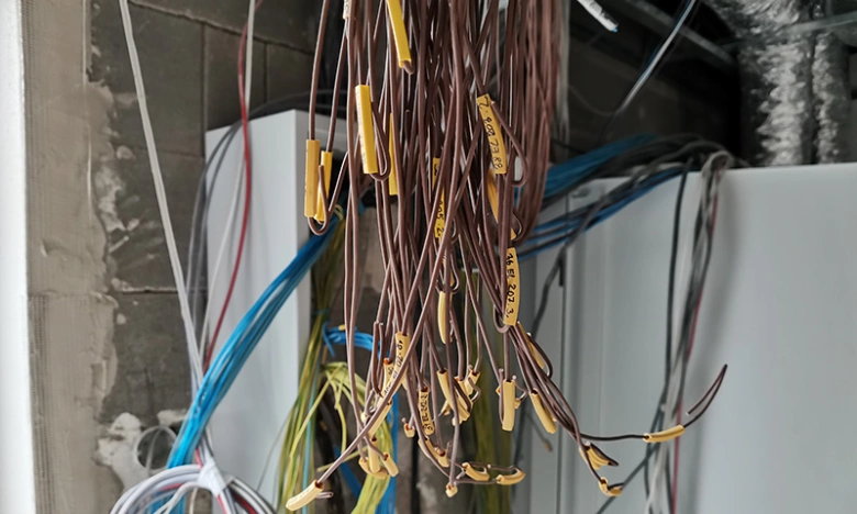 Hromadný svazek označených elektrických kabelů visících v instalaci.