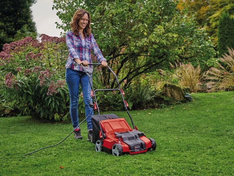 Žena kosí trávník červenou elektrickou sekačkou.