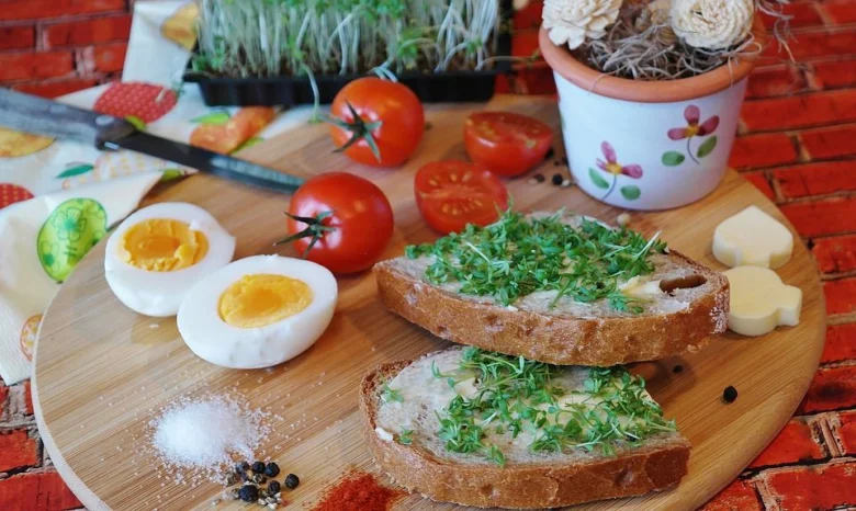 Kráje chleba s řeřichou, vejcem a rajčaty na dřevěném talíři.