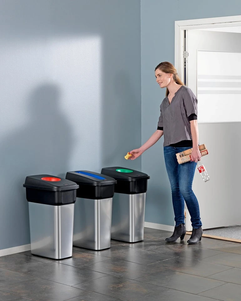Žena třídí odpad do barevných kontejnerů na recyklaci.
