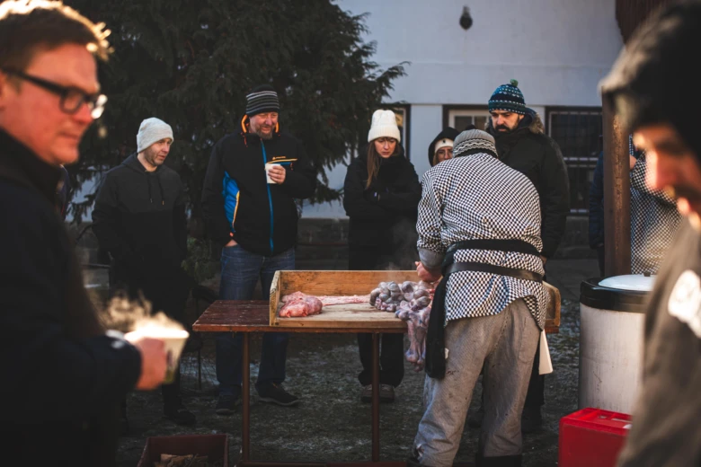 Tradiční zabijačka prasete venku s lidmi kolem.