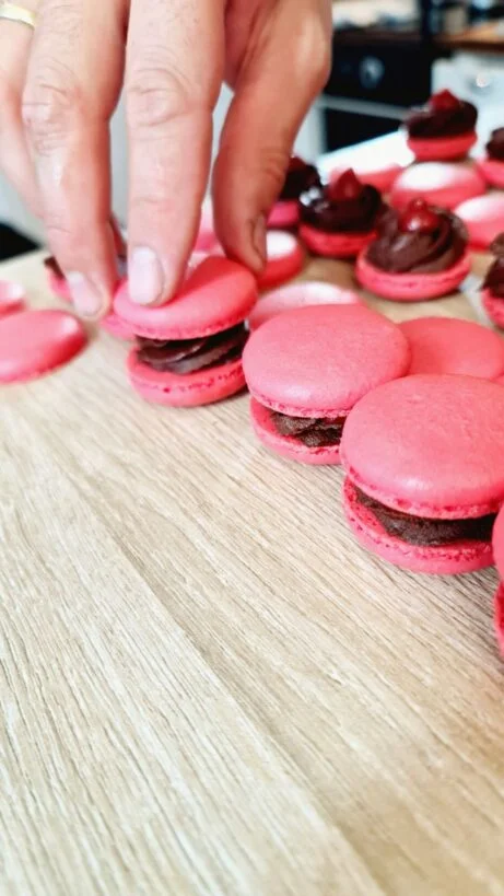 Růžové makarony s čokoládovou náplní na dřevěném povrchu.