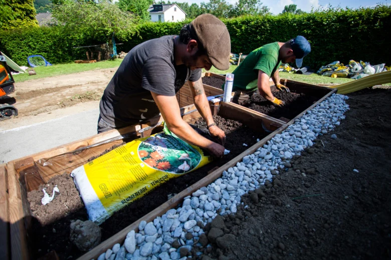 Dva lidé připravují půdu pro balkónové květiny v dřevěných nádobách.
