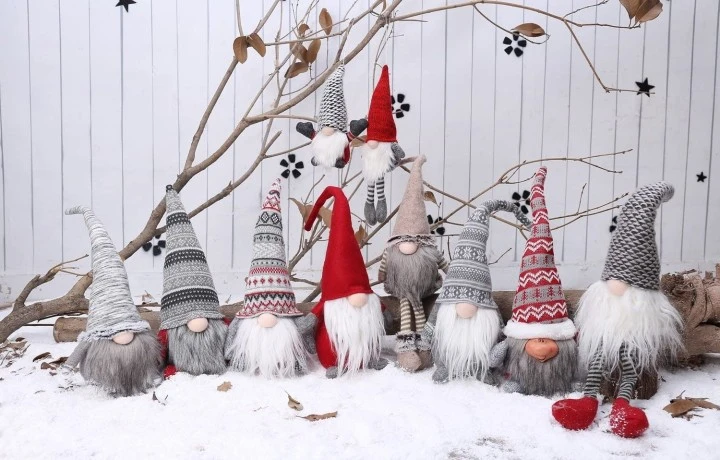 Skupina vánočních trpaslíků v sněhu před bílou plotem.